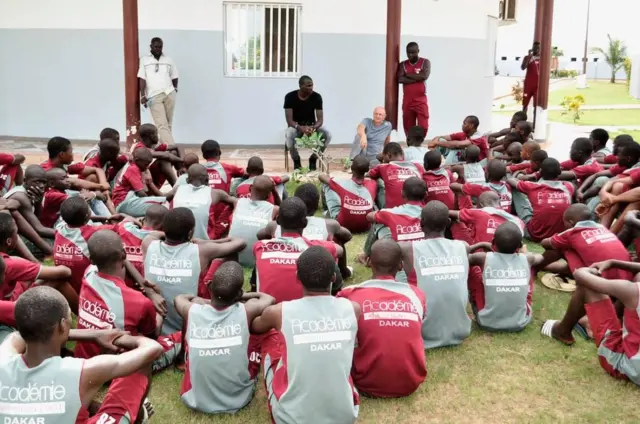 young football players aged 12-14 sitting on the ground listening to coaches